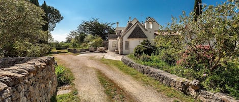 A stone-walled path leading to a building with a steeply pitched roof and a small bell tower.