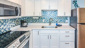 A compact kitchen with white cabinetry, a stainless steel sink, a coffee maker, and a microwave.
