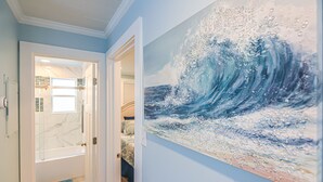 A hallway with a large wave painting on the wall, a door leading to a bathroom, and a blue bench.