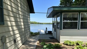 Una terraza de madera que conduce a un muelle, un espacio cubierto pequeño con ventanas y vistas a un lago.