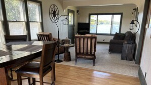 Un salón amplio con un gran ventanal, una zona de comedor con mesa y sillas de madera, y una acogedora sala de estar con sofá y sillones.