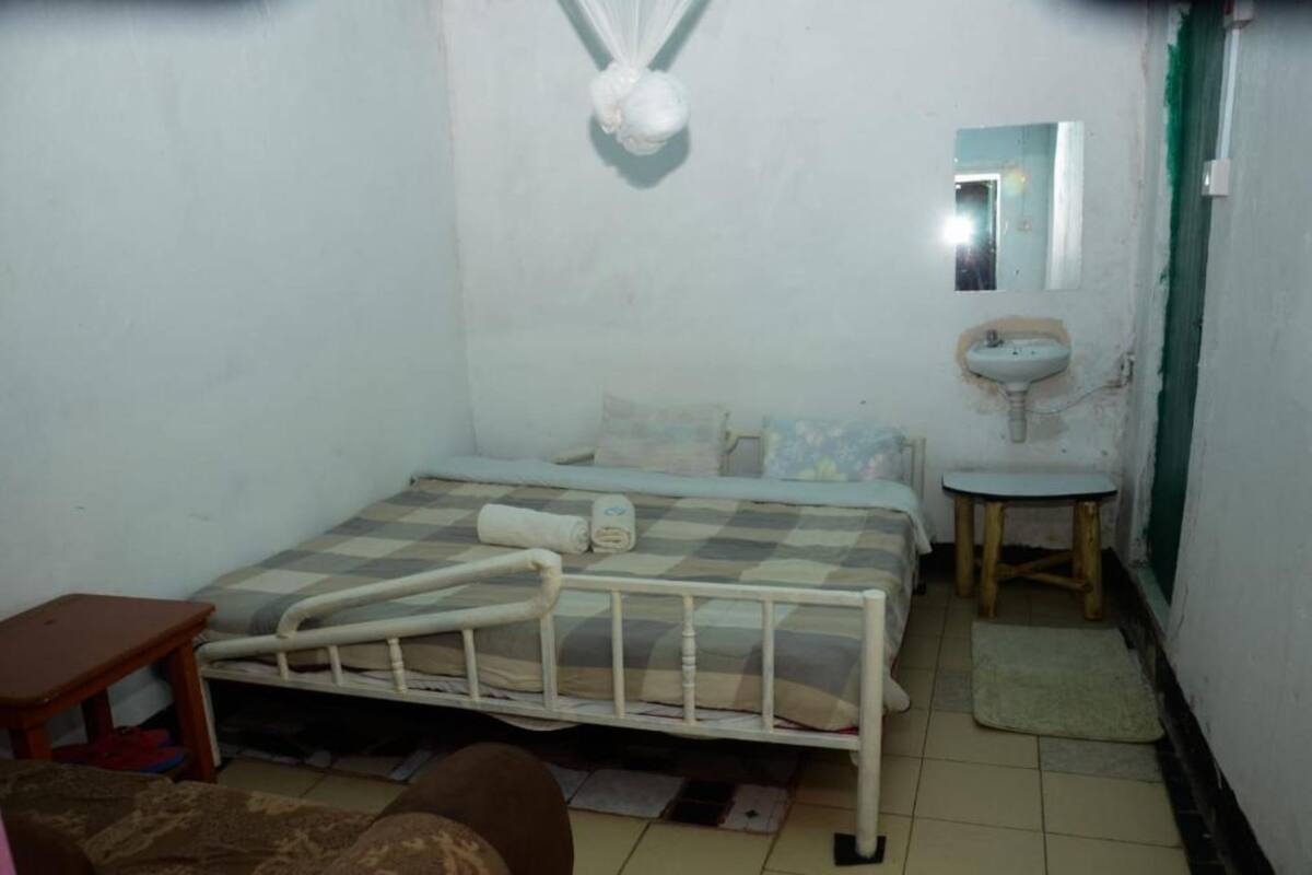 Habitació petita i senzilla amb un llit sol, una taula petita, una tauleta de nit, un mirall i un rentapans.