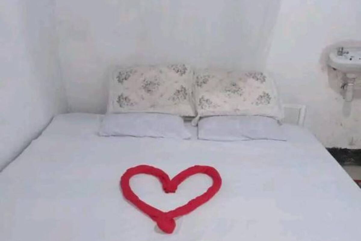 Un llit amb una decoració en forma de cor al matalàs, un panell de capçal blanc i una taula de nit amb un rentapeus.