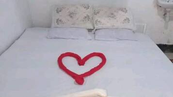 Una cama con una decoración en forma de corazón sobre el colchón, un cabecero blanco y una mesita de noche con un lavamanos.