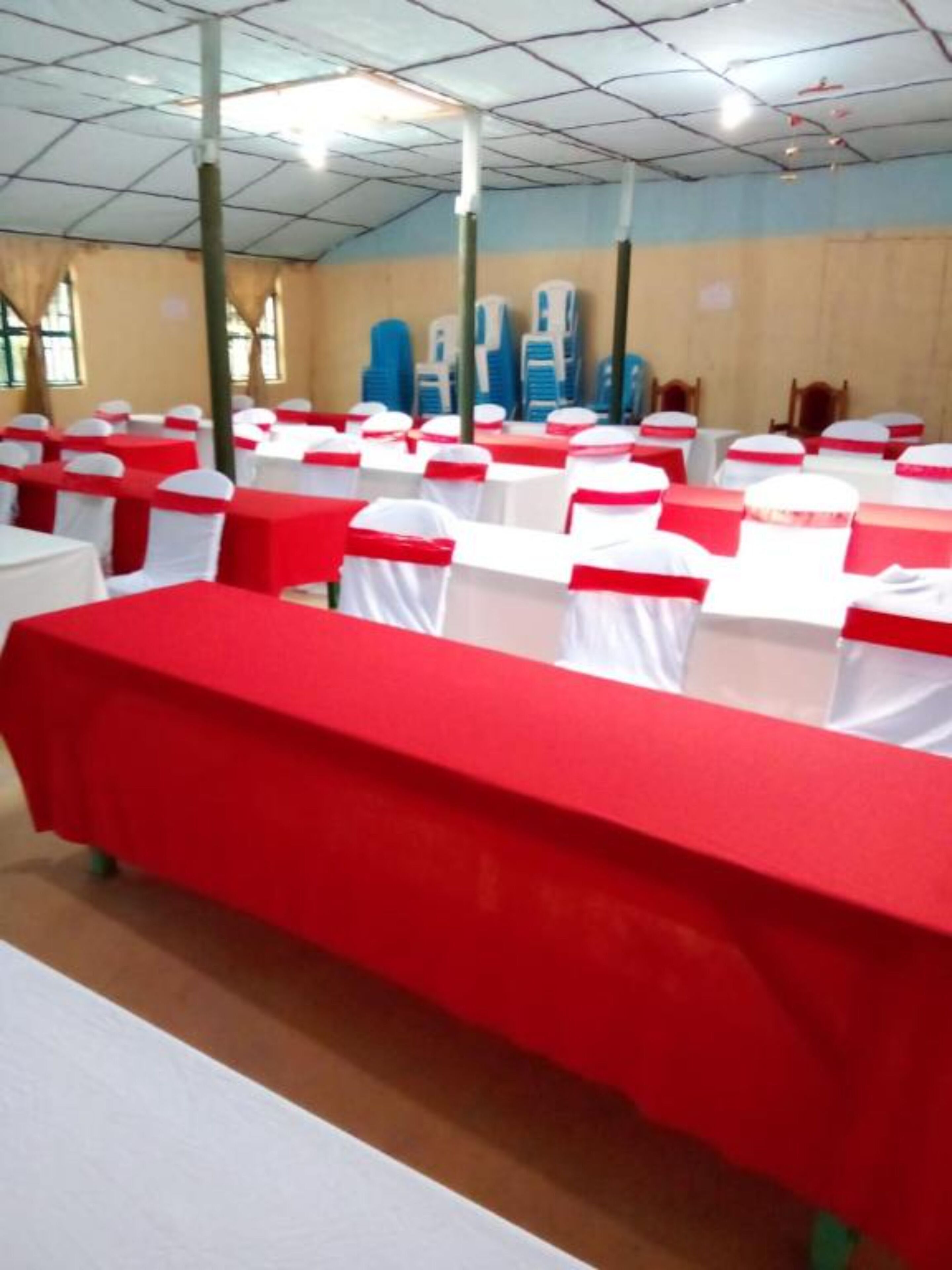 A conference room with rows of tables covered in red tablecloths and white chairs with red sashes.