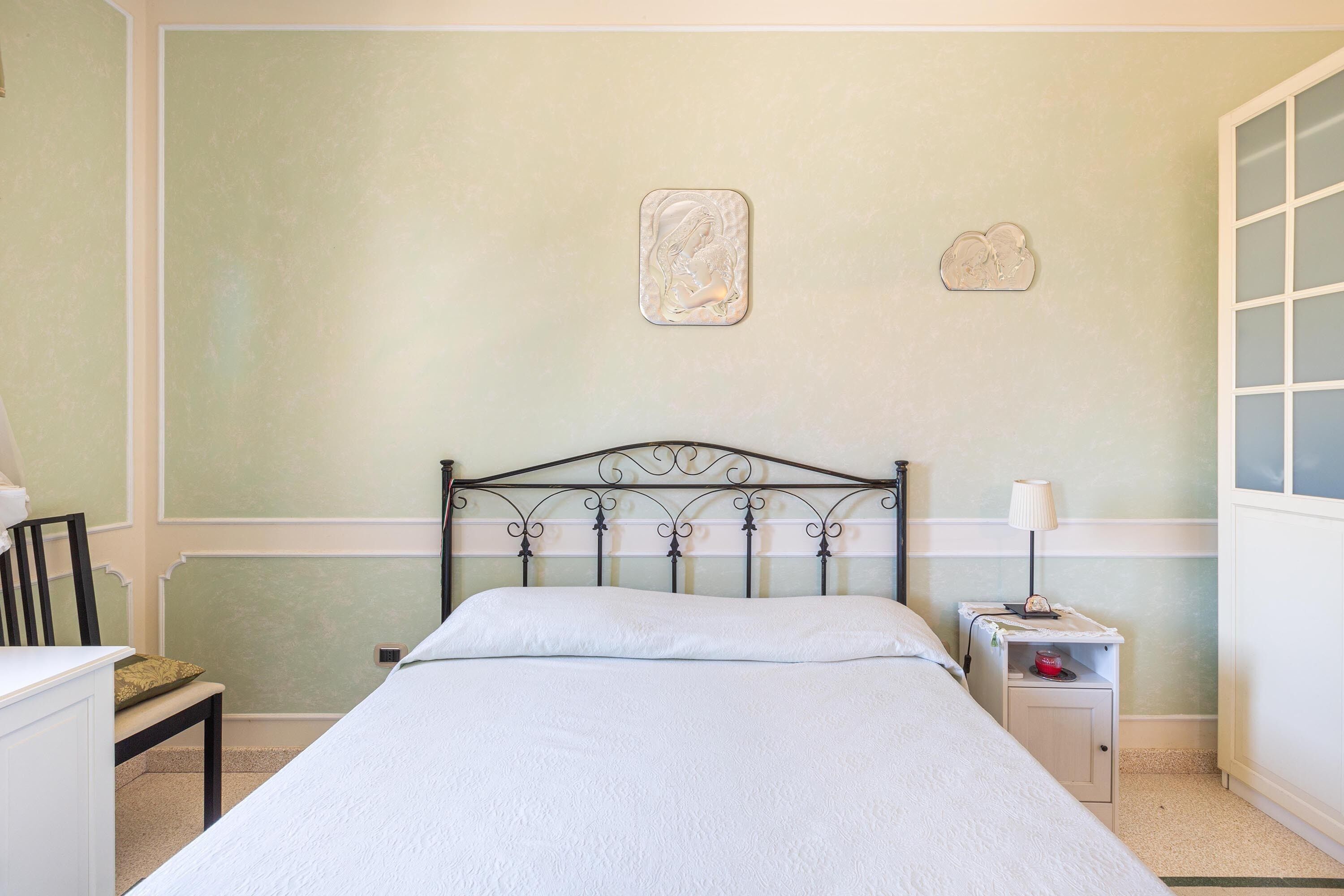 A bedroom with a bed, a nightstand, a chair, and a wall-mounted artwork.