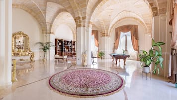 A spacious lobby with a large, ornate rug, a grand piano, and a bookshelf.