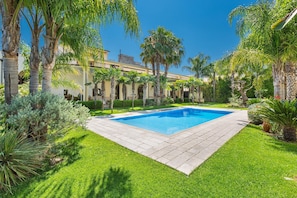 Piscina rodeada de césped cuidado y palmeras, con un edificio al fondo.