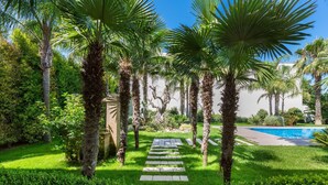 Un sentier qui mène à une piscine entourée de palmiers et d’une végétation luxuriante.
