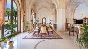Un vaste espace dédié à la salle à manger, avec une longue table et des chaises, le tout entouré de murs en pierre en forme d’arc et de grandes fenêtres.