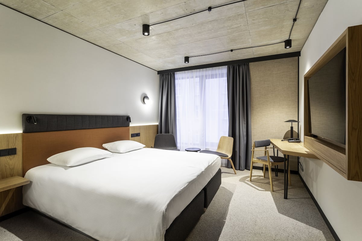 A hotel room with a large bed, a desk with a chair, a TV, and a window with curtains.