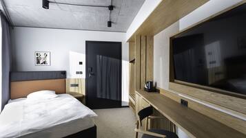 A modern hotel room with a bed, a desk, a chair, a large TV, and a door leading to another room.
