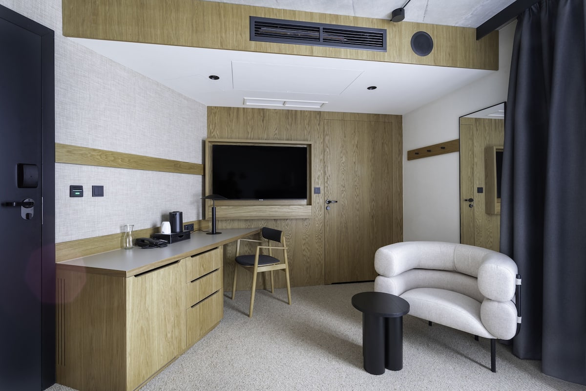 A compact hotel room with a wooden desk, a chair, a sofa, a television, and a small table.