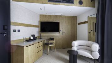 A compact hotel room with a wooden desk, a chair, a sofa, a television, and a small table.