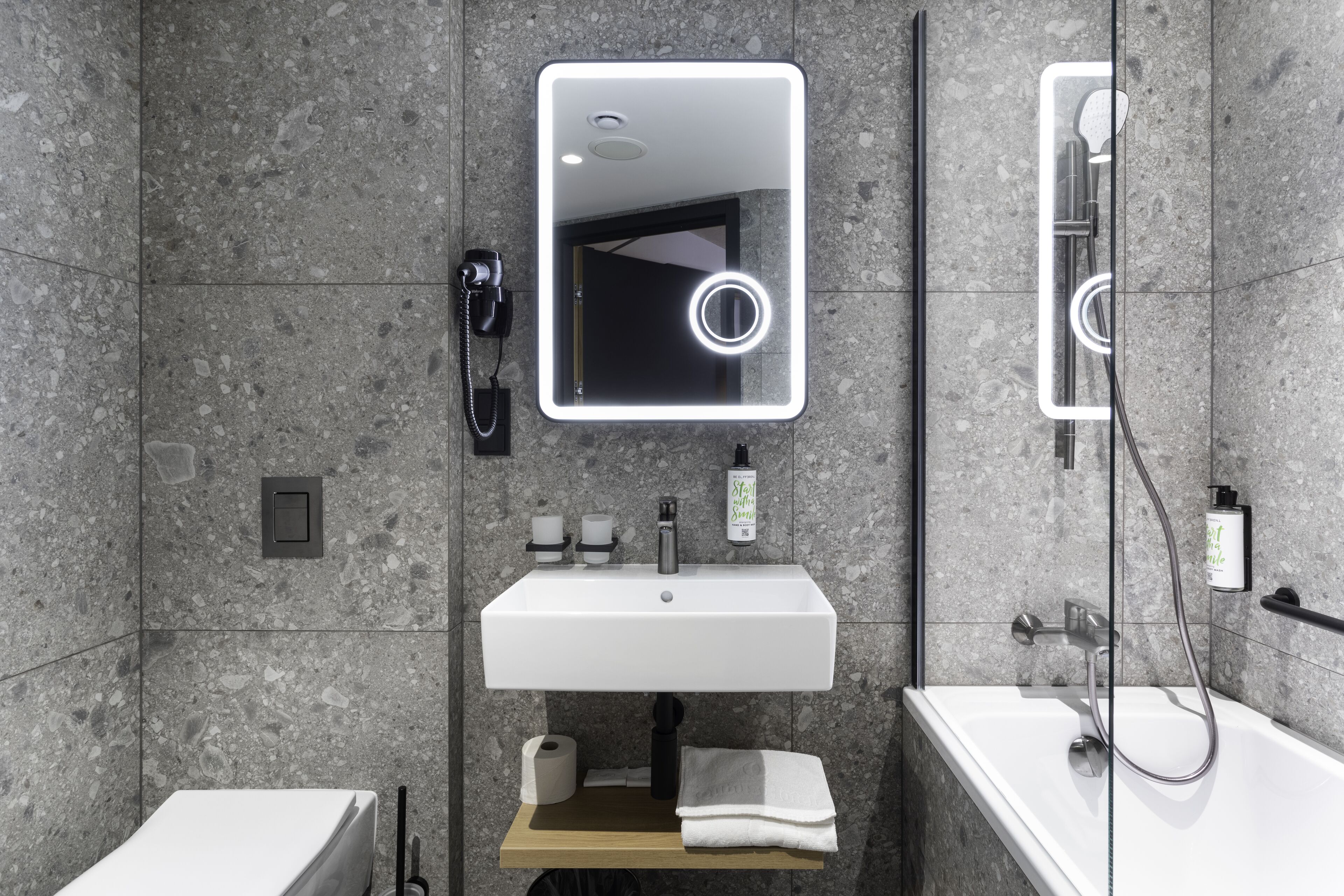 Un bagno moderno con un lavandino bianco, uno specchio con illuminazione integrata, una doccia e un water.