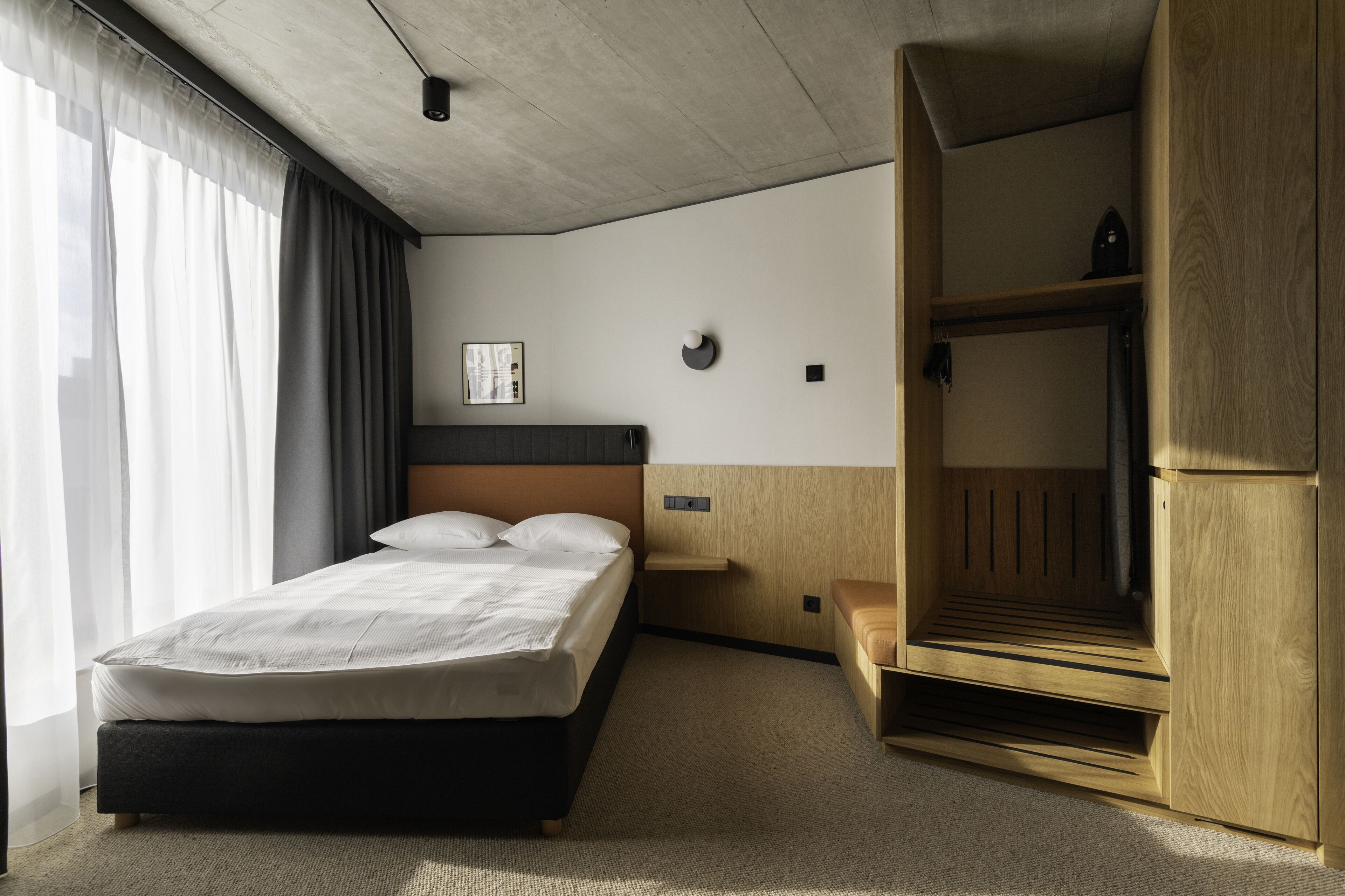A modern hotel room with a bed, wooden wardrobe, and a small bedside table.