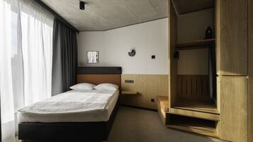 A modern hotel room with a bed, wooden wardrobe, and a small bedside table.