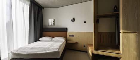 Una habitación de hotel moderna con una cama, un armario de madera y una mesita de noche.