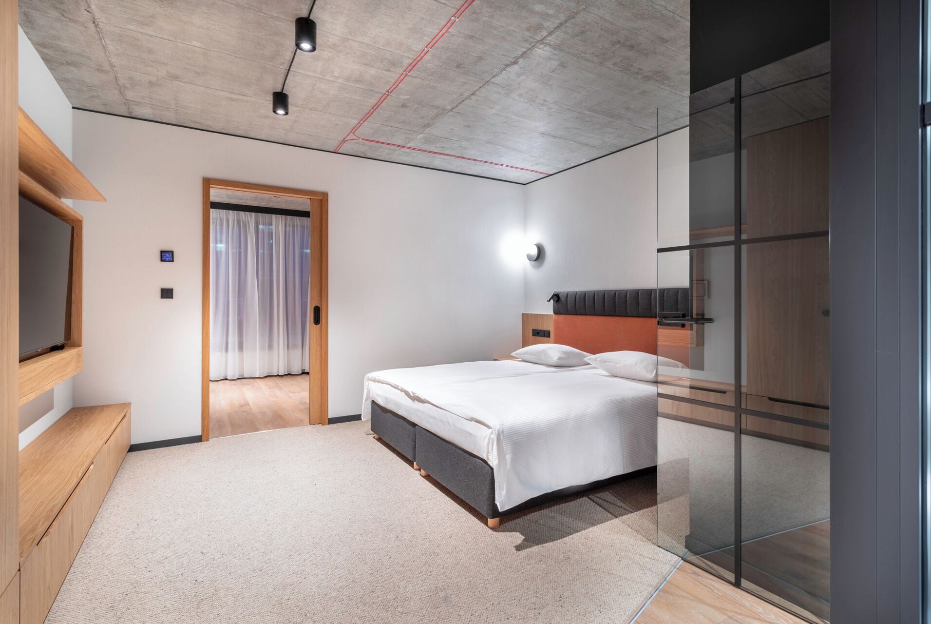 Ein modernes Hotelzimmer mit einem großen Bett, einem an der Wand montierten Fernseher und einer Glastrennwand.