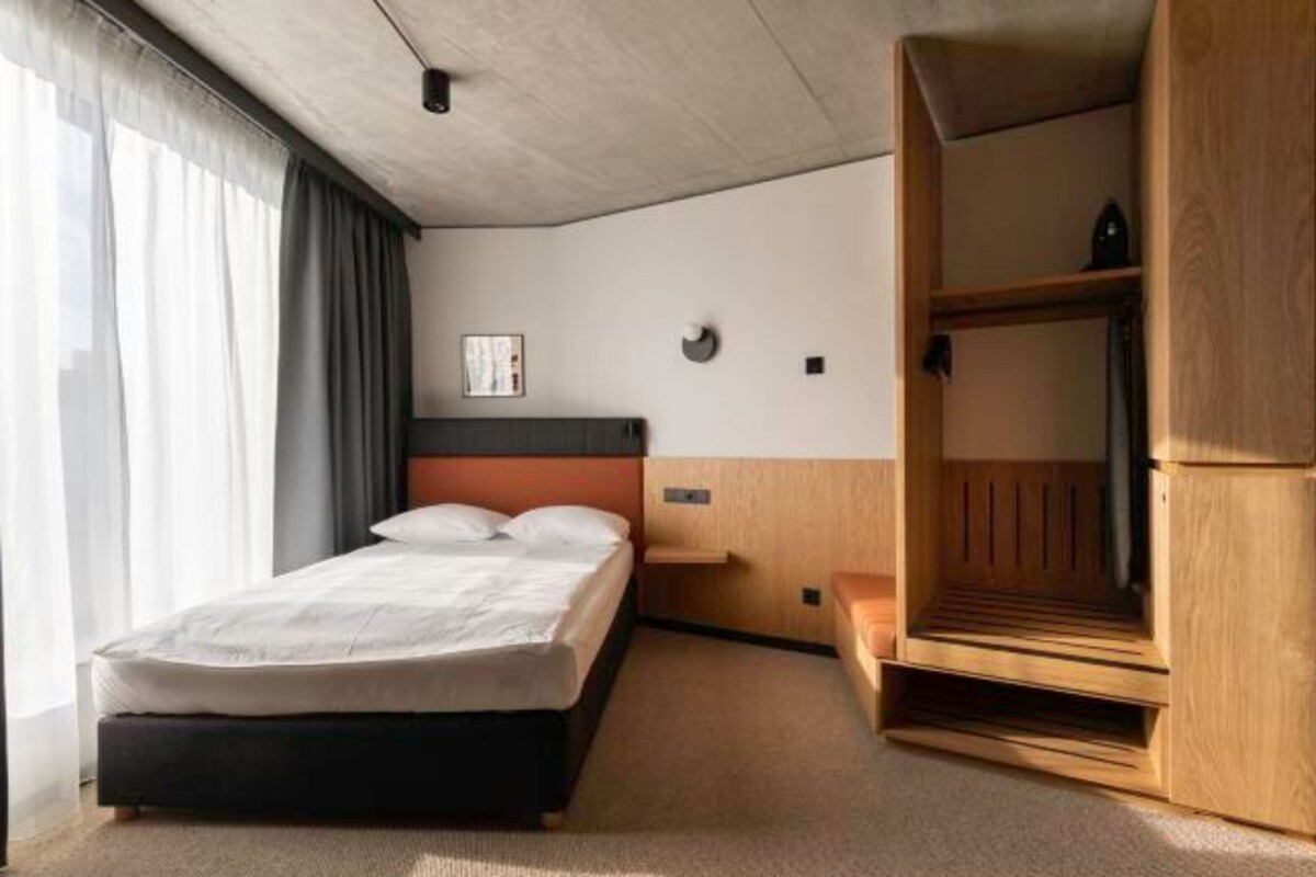 A modern hotel room with a bed, a wooden bench, and a built-in wardrobe.