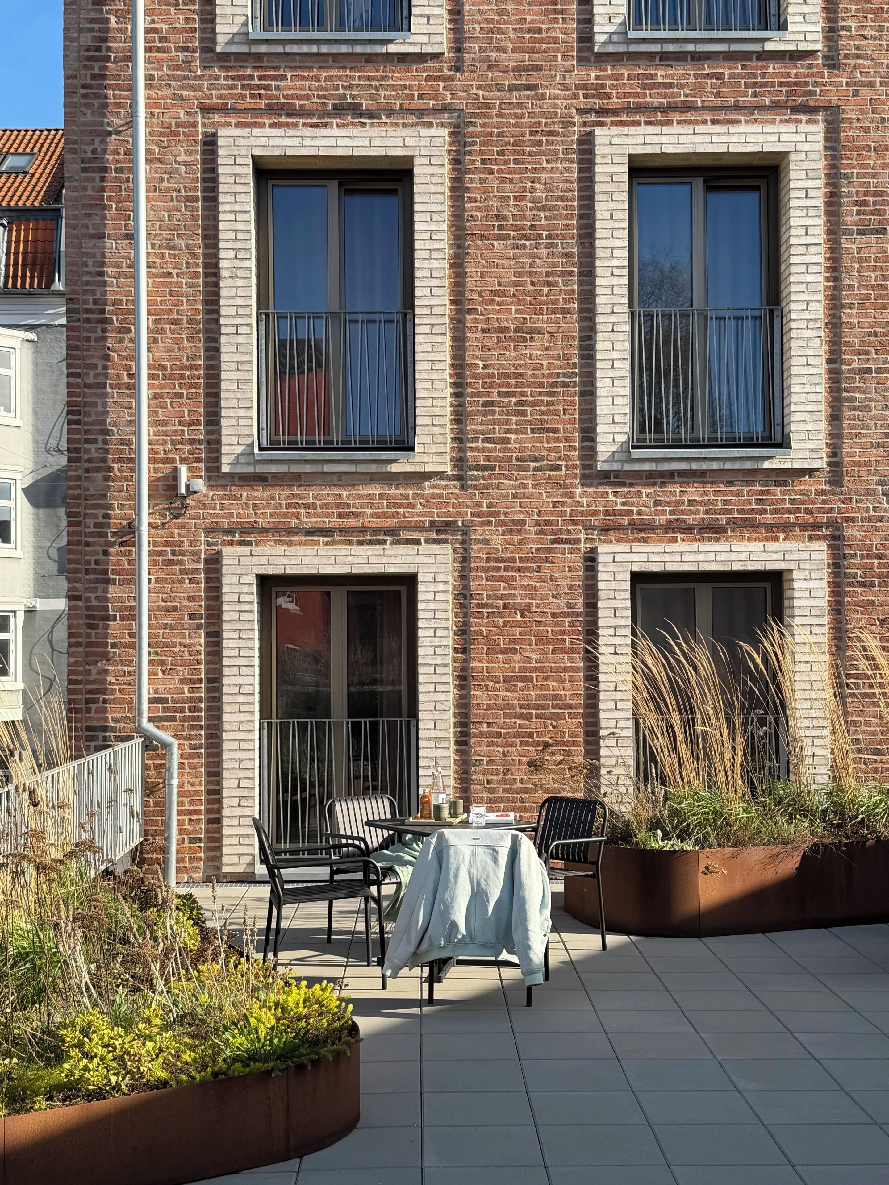 A multi-story building with a brick facade, outdoor seating area with a table and chairs, and a planter with plants.