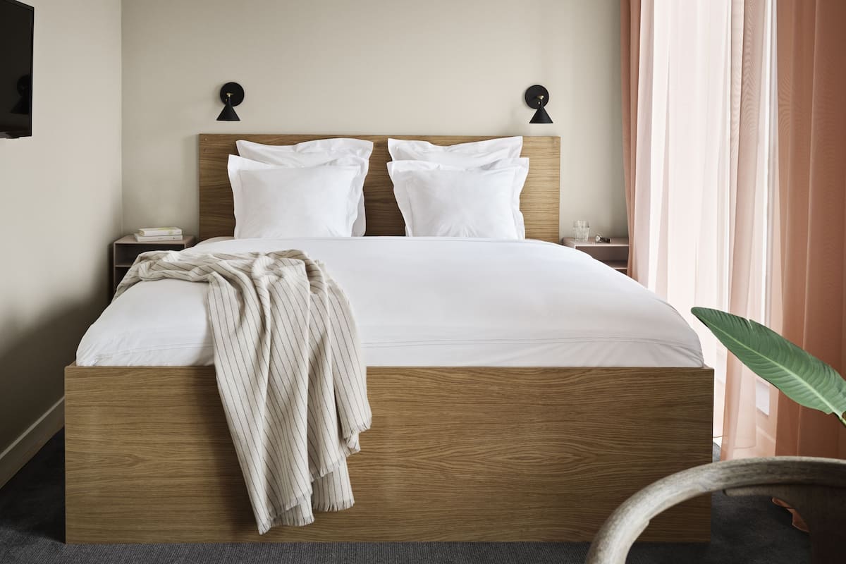 A neatly made bed with a wooden headboard, white bedding, and a throw blanket.