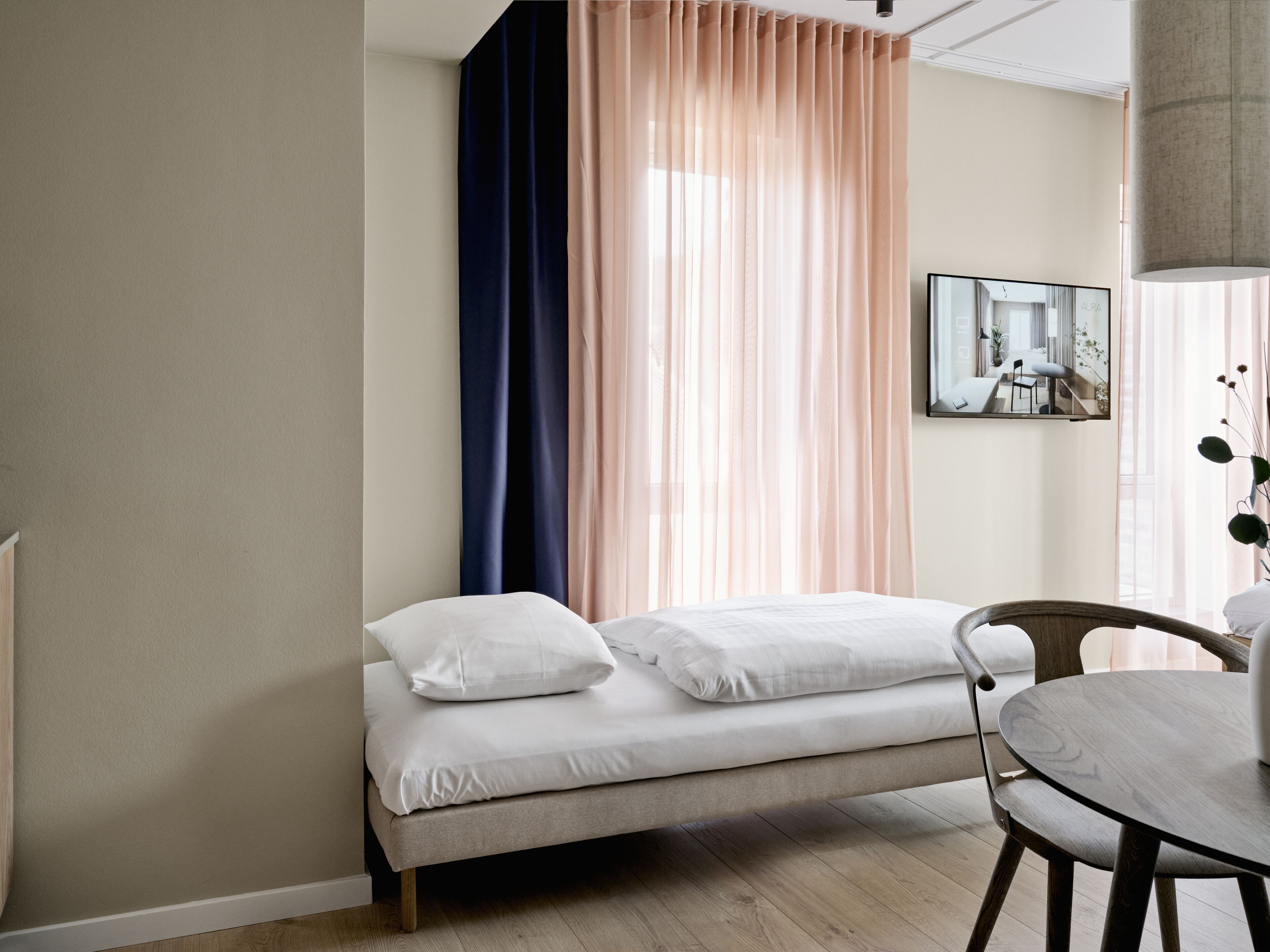 A modern bedroom with a bed, a round dining table, and a view of a room through a window.