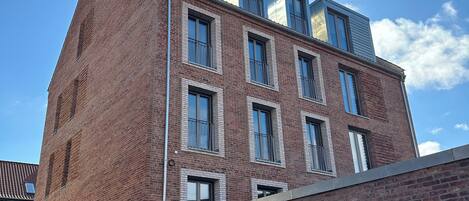 A multi-story building with a mix of brick and modern glass elements, featuring multiple balconies and large windows.