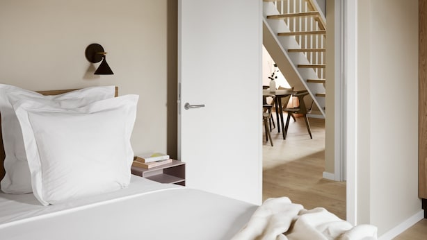 Un dormitorio con una cama, una mesita de noche, una puerta que da a una escalera y vistas a un comedor.