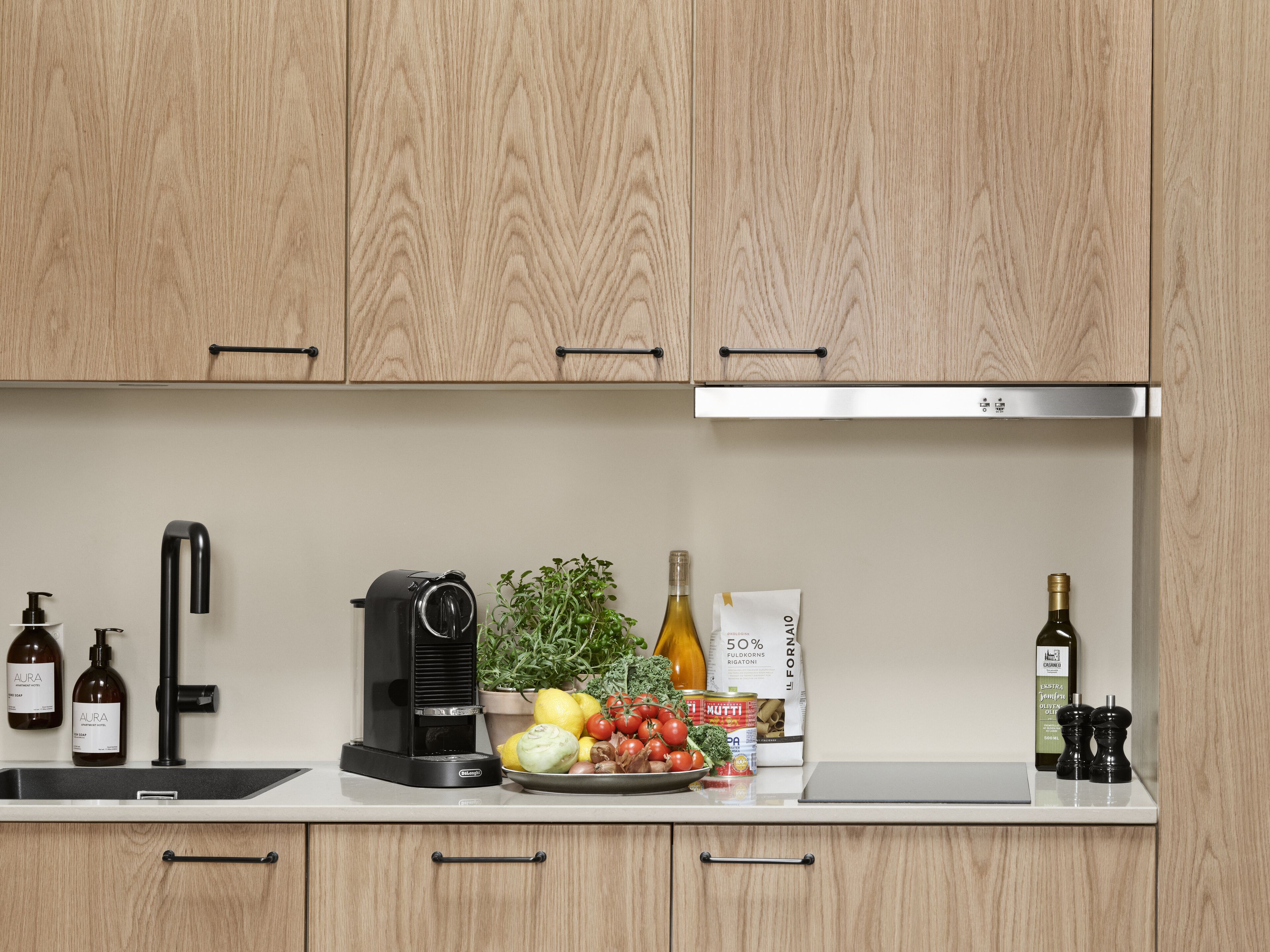 Una cocina con armarios de madera, una campana extractora de acero inoxidable, una cafetera, un lavabo y diversos alimentos sobre la encimera.