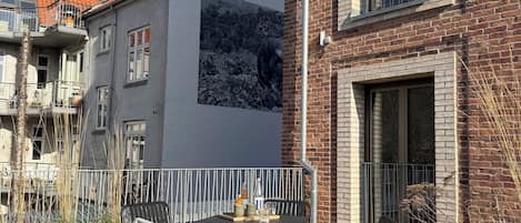 An outdoor seating area with a table and chairs, a potted plant, and a building with a mural.