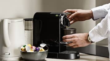 Una cocina con una cafetera, un bol de cápsulas de café y una persona preparando café.