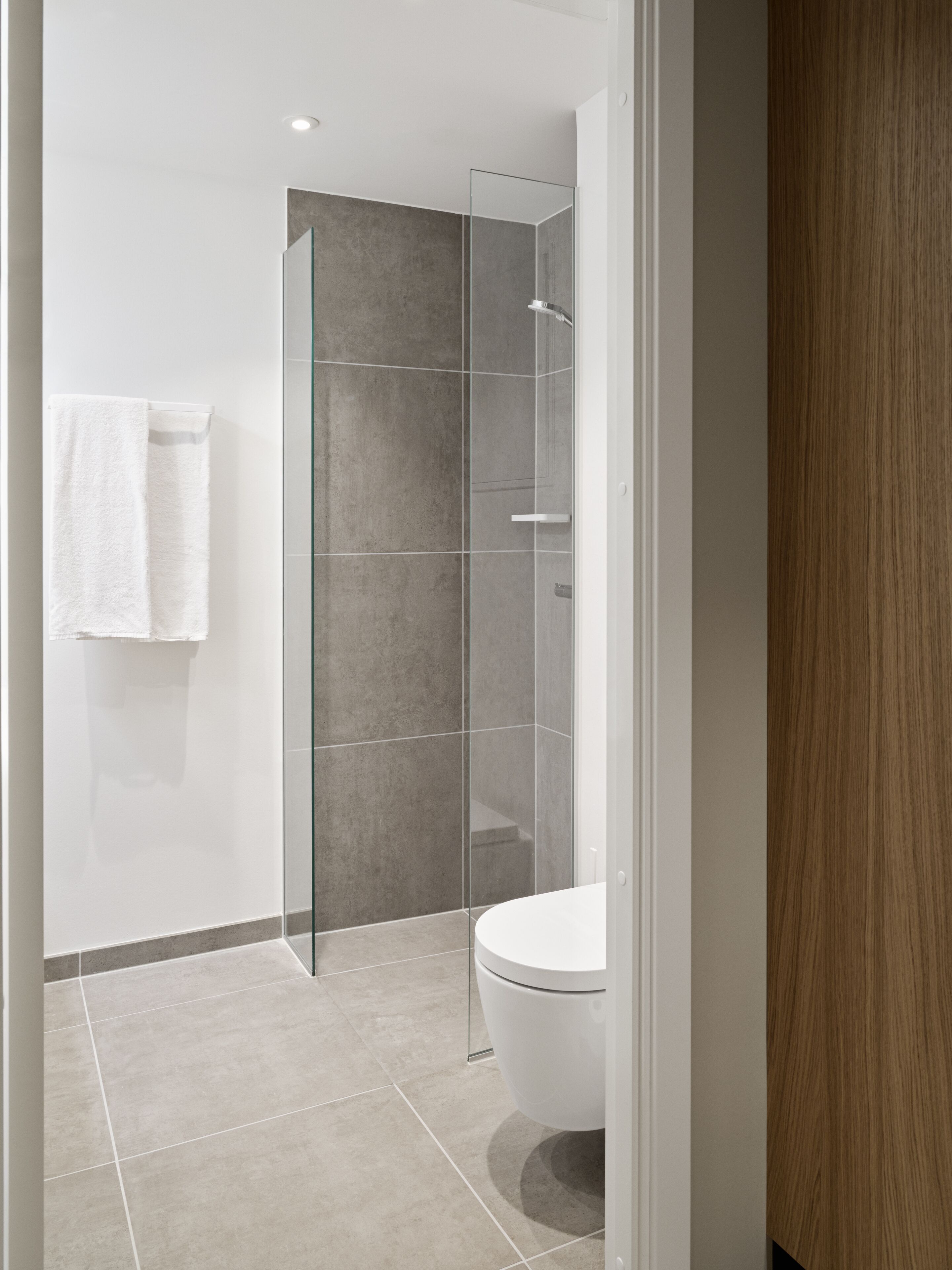 Un baño moderno con ducha de mampara de vidrio, inodoro y perchero para toallas.