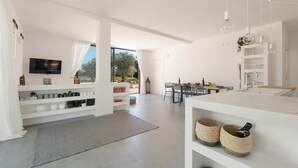 A modern, open-plan living and dining area with a flat-screen TV, white shelving, and a dining table with chairs. - 3538 Villa Sylvia by Perle di Puglia (San Vito dei Normanni)