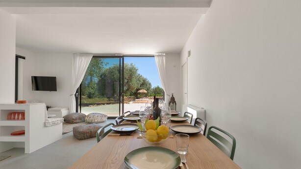 A modern dining area with a wooden table set for four, a bowl of lemons, and a view of the outdoors through large windows. - 3538 Villa Sylvia by Perle di Puglia (San Vito dei Normanni)