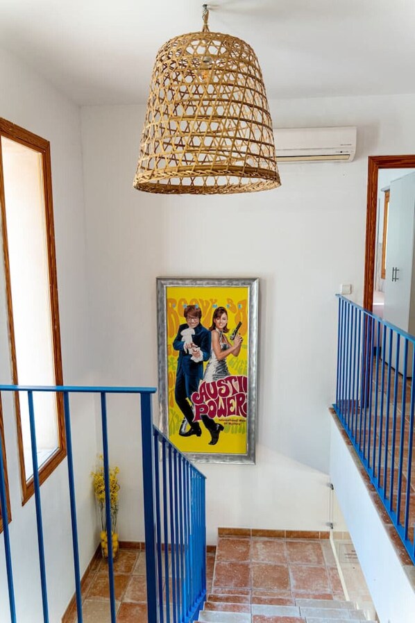 A staircase with blue railings, a woven ceiling light fixture, and a framed poster on the wall.