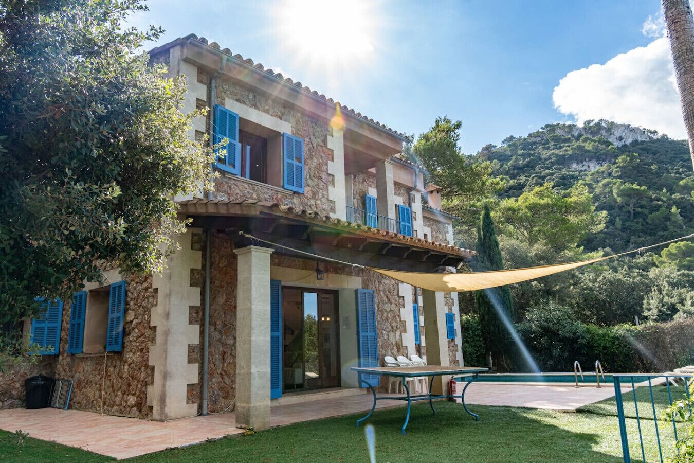 A two-story house with stone walls and blue shutters, a pool, and a grassy yard.