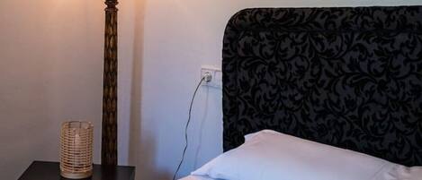Un lit bien fait, avec du linge de lit blanc, une lampe rouge sur une table de chevet et une tête de lit à motifs.