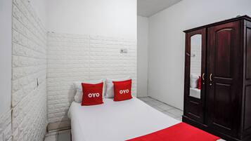 A bedroom with a white brick wall, a wooden wardrobe, and two red pillows with the word 'OYO' on them.