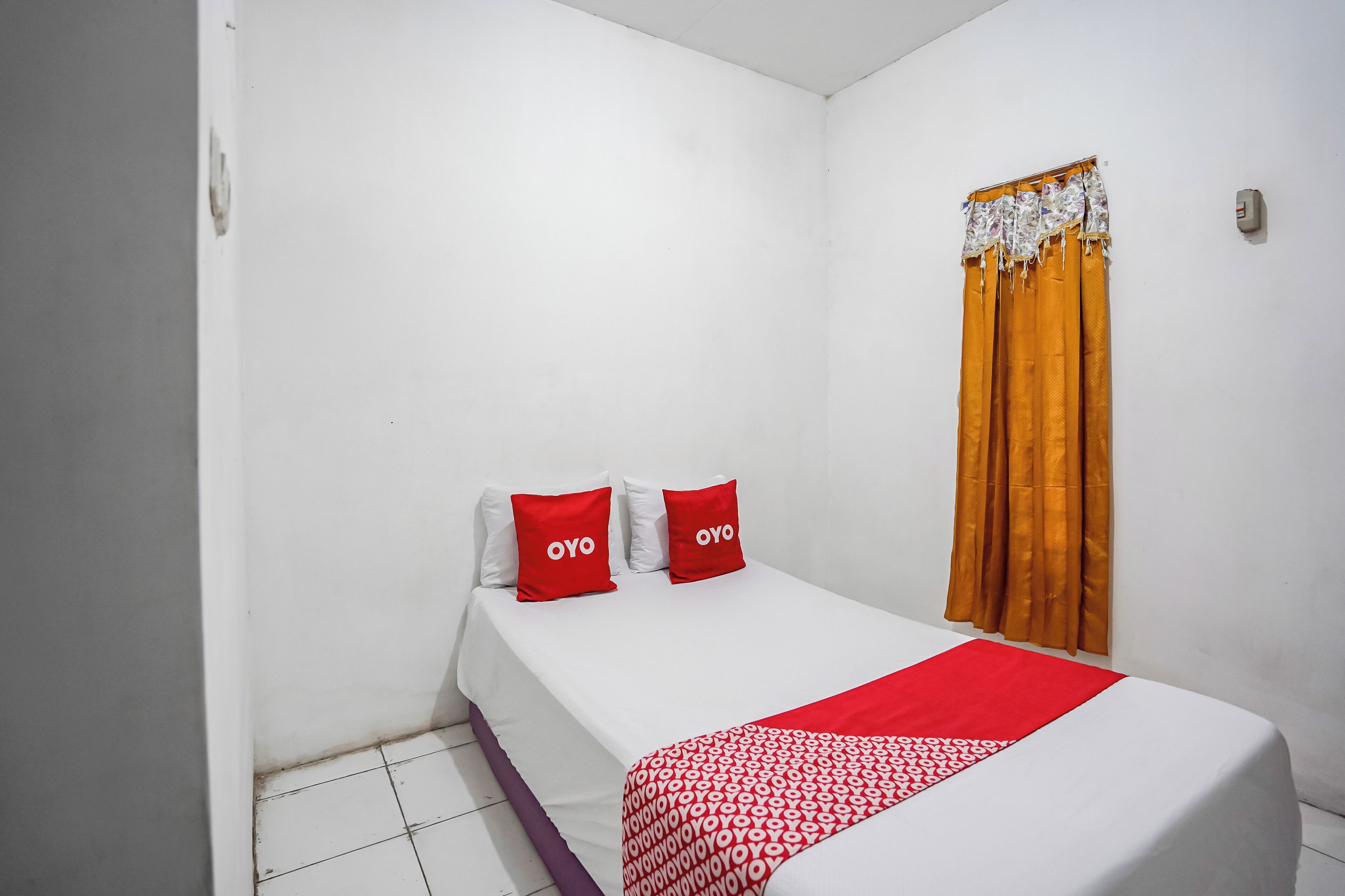 A small, single-bed room with white walls, a white bedspread, and two red pillows with the word 'OYO' on them.