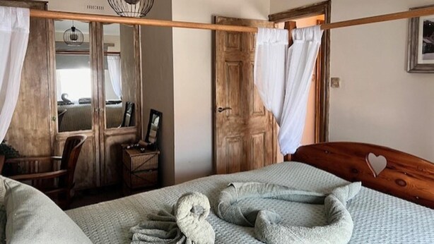 A bedroom with a bed, a wooden headboard, a hanging light fixture, a mirror, and a door with curtains. - Historic Countryside Cottage - Sleeps 3 & Pets Ok (Morecambe)