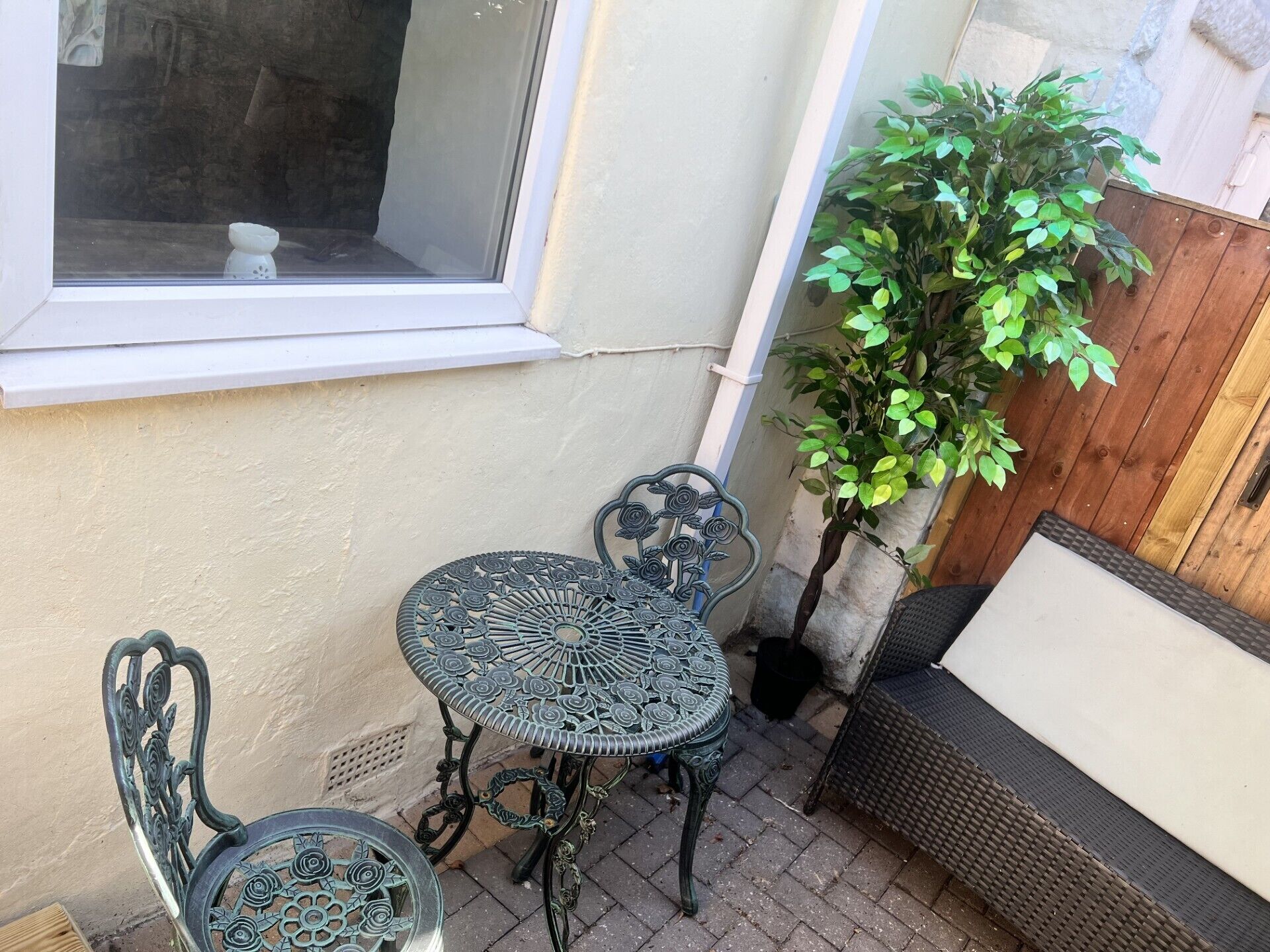 A small patio area with a metal table and chairs, a potted plant, and a window.