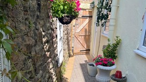 A narrow stone-walled alley with a wooden door, potted plants, and a window. - Historic Countryside Cottage - Sleeps 3 & Pets Ok (Morecambe)
