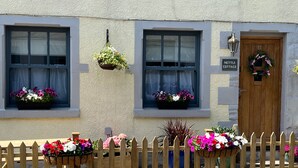 A cottage with a wooden door, two windows with hanging flower baskets, and a picket fence. - Historic Countryside Cottage - Sleeps 3 & Pets Ok (Morecambe)