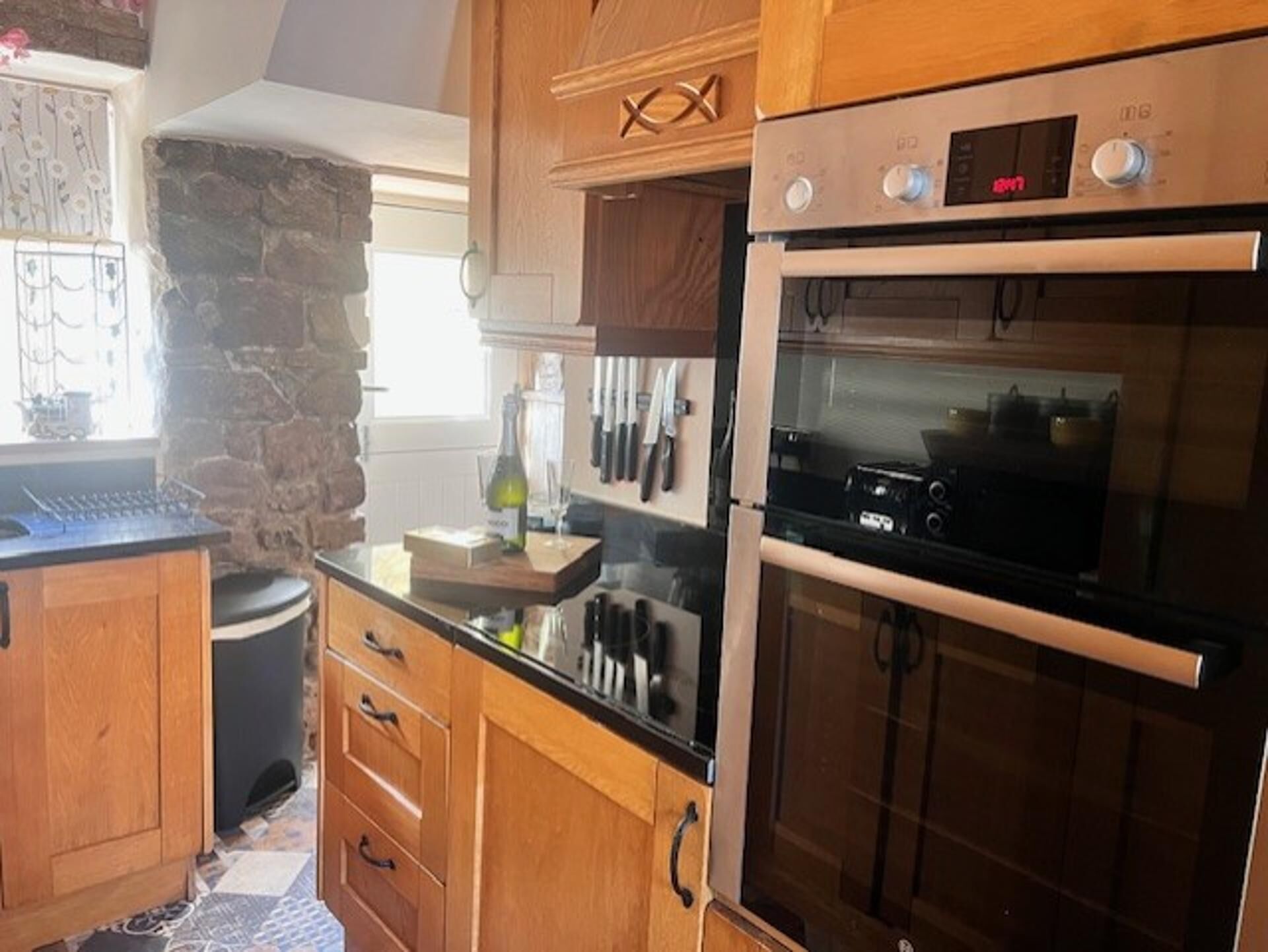 A kitchen with wooden cabinets, a stone wall, and a built-in oven.