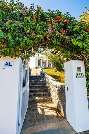 Una escalera conduce a un edificio de fachada blanca, con una puerta que indica 'AL' (Alojamiento local) y un letrero 'D10' en la pared.