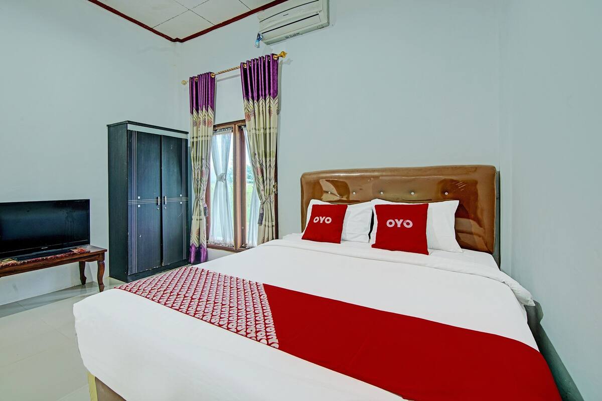 A hotel room with a bed, a television, a wardrobe, and curtains.