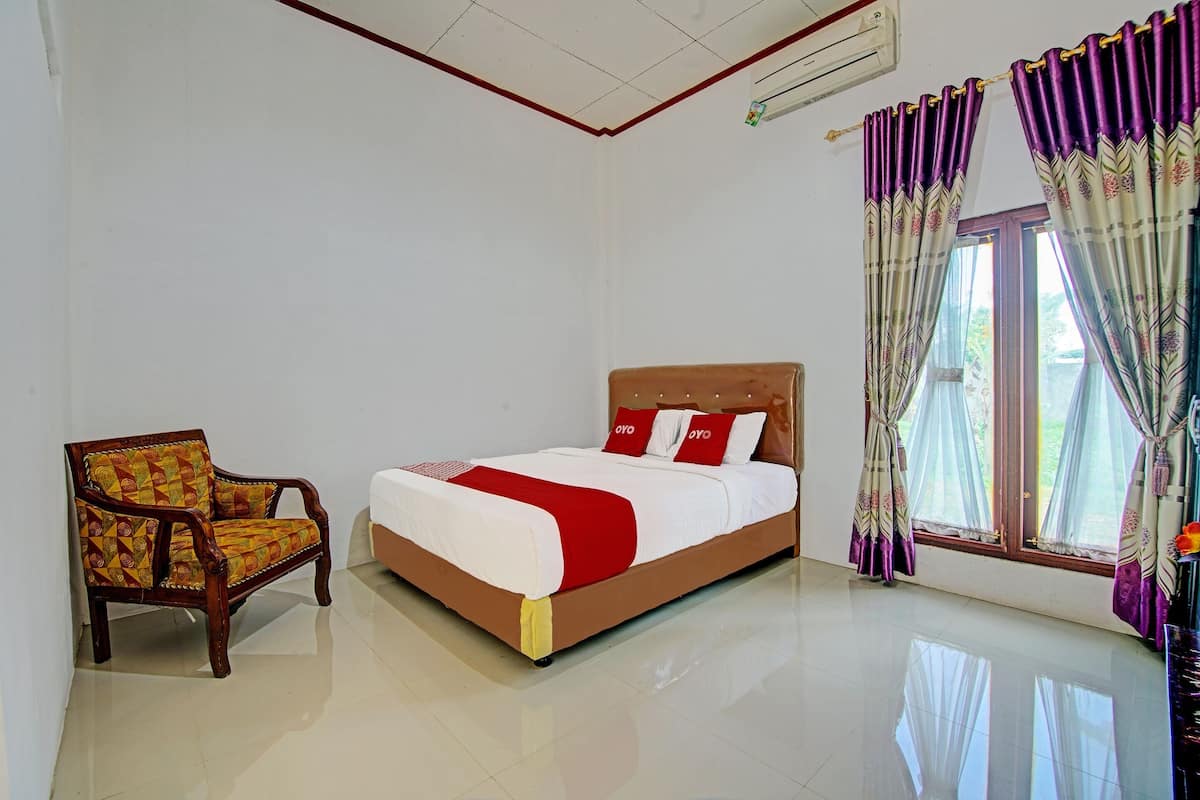A bedroom with a bed, a chair, and a window with curtains.