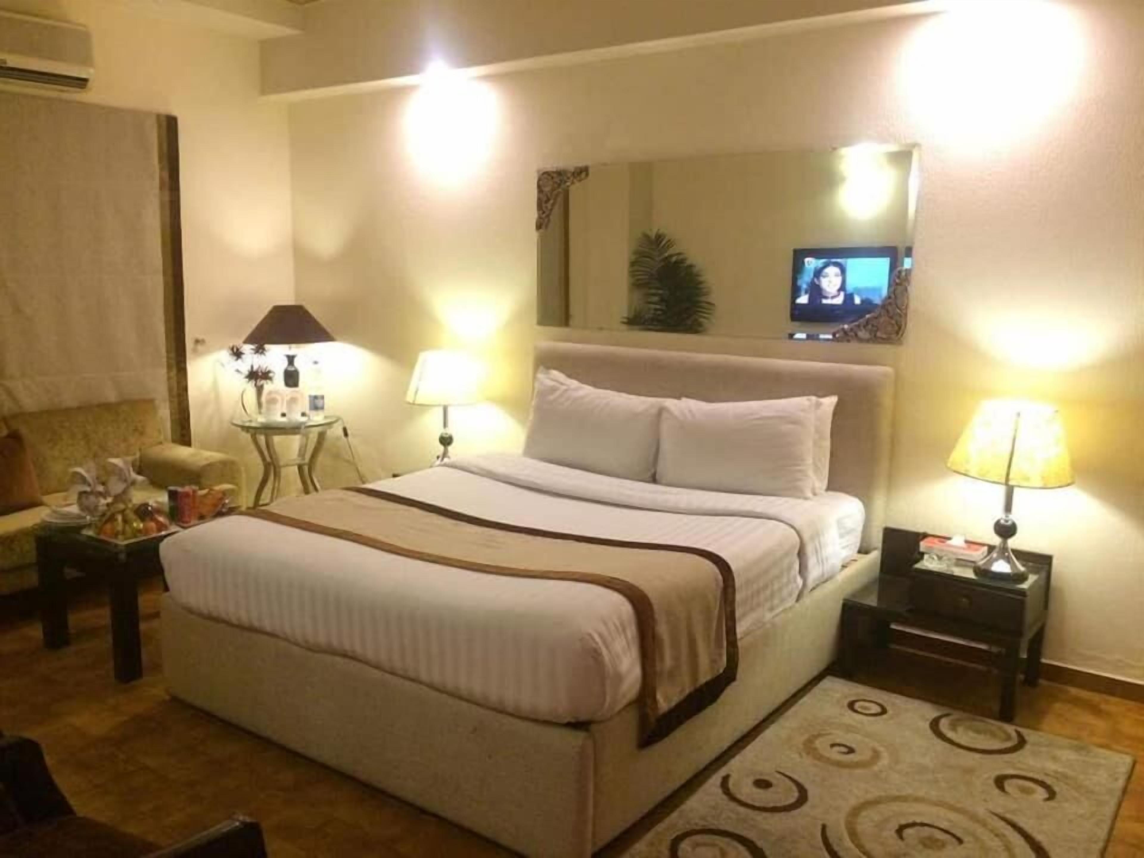 A hotel room with a bed, two bedside tables, a TV, a lamp, a sofa, and a carpet.