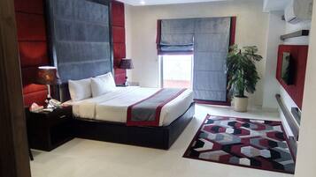 A modern bedroom with a large bed, a nightstand, a lamp, a potted plant, and a geometric rug.